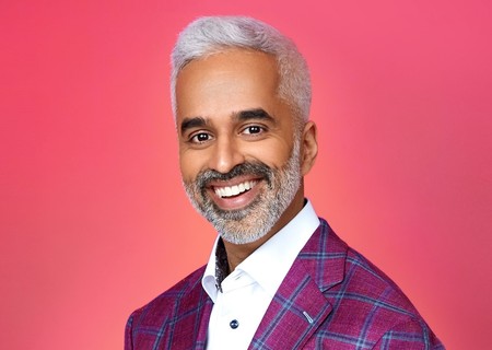 Professional headshot of Riaz Meghji, innovation keynote speaker, wearing purple plaid blazer against coral background